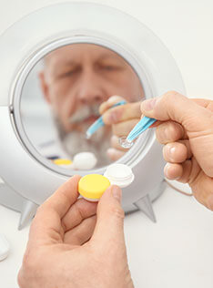 Man in front of a mirror holding a contact lens