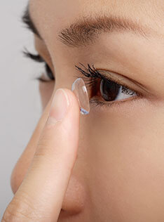 A woman putting on a contact lens to her eye